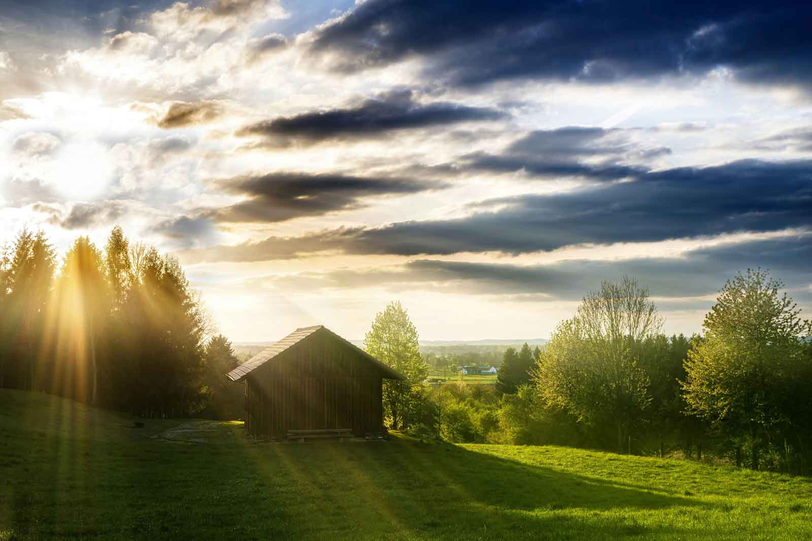 shed on a green hill with sun beams shining through the clouds